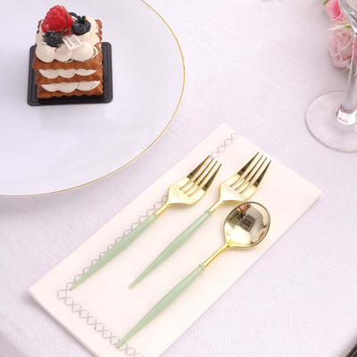 Elegant gold and green cutlery set on a napkin with a dessert in the background.