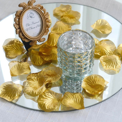 Glass candle holder surrounded by gold petals on a mirrored surface.