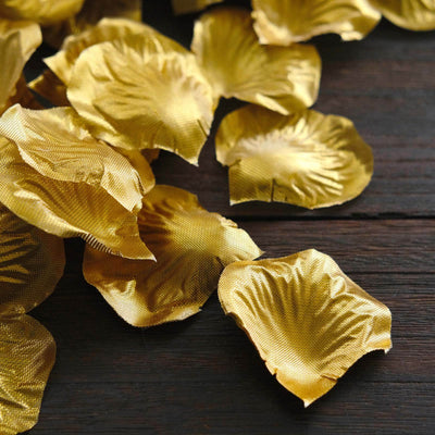 Golden silk rose petals scattered on a rustic wooden surface.