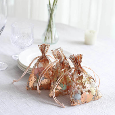 Three decorative favor bags filled with pastel candies on a table.