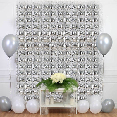 Silver balloon backdrop with white and silver balloons and a floral arrangement.
