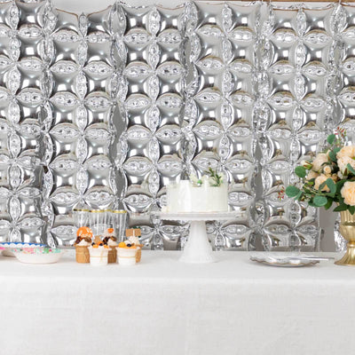Elegant dessert table with silver balloon backdrop and floral arrangements.