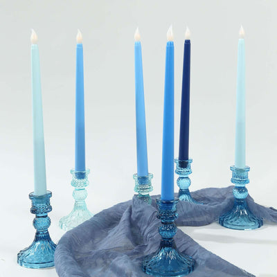Blue and teal candles in elegant glass holders on a soft fabric backdrop.