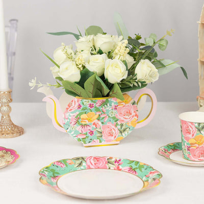 Floral teapot arrangement with roses and greenery on a table setting.