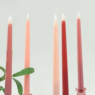Colorful tapered candles in shades of pink and red with greenery.