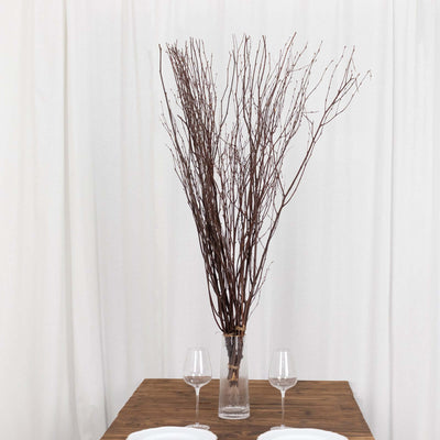 Dried branches in a vase on a wooden table with wine glasses