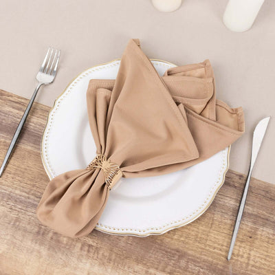 Elegant beige napkin tied with a decorative ring on a white plate.