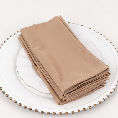 Set of four beige cloth napkins neatly stacked on a decorative plate.