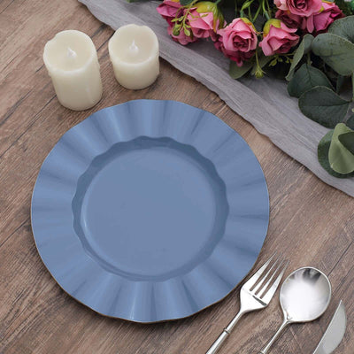 Blue scalloped dinner plate with silver utensils and candles on a wooden table.