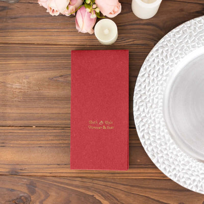 Red wedding invitation on a wooden table with flowers and a decorative plate.