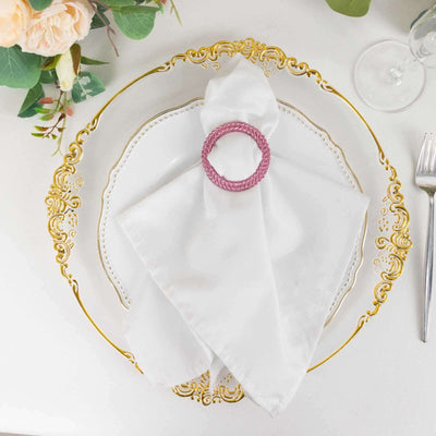 Elegant white napkin with pink napkin ring on ornate gold plate.