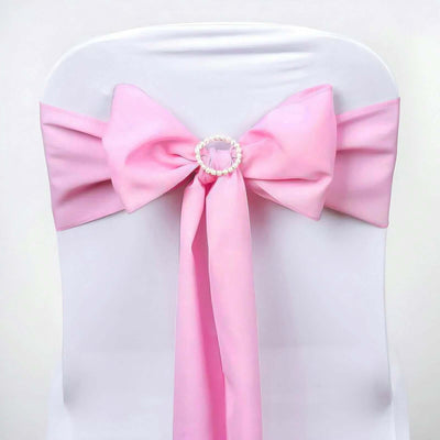 Pink satin chair bow with pearl ring embellishment on a white chair.