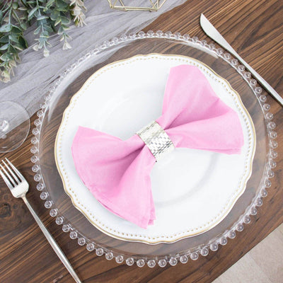 Pink bow napkin on a decorative plate with a clear charger on a wooden table.