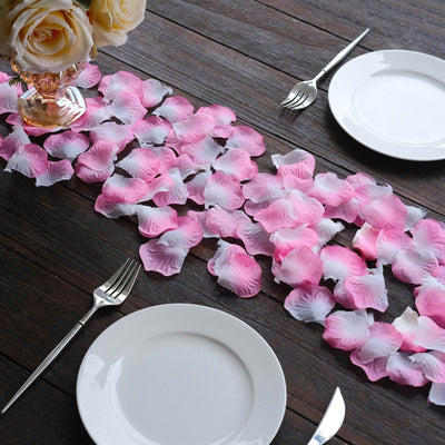 Pink and white rose petals arranged on a table with dinner plates and forks.