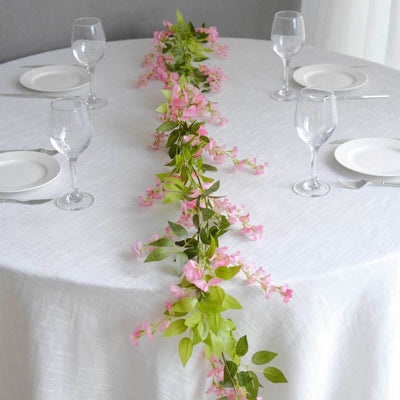 Pink floral table runner on a white tablecloth with wine glasses and plates.