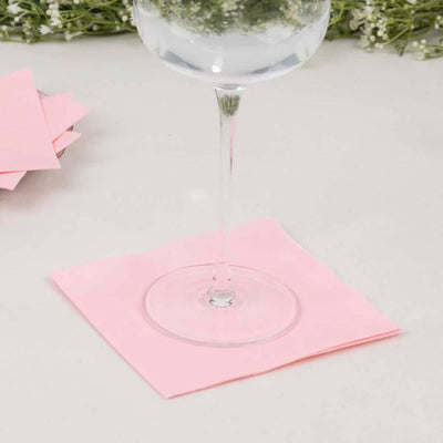 Pink cocktail napkin under a glass of water on a neutral surface.