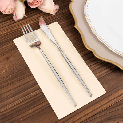 Silver fork and knife set on a beige napkin with floral decor.