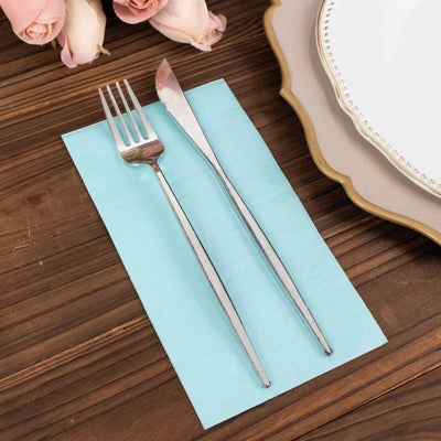 Silver fork and knife on a turquoise napkin with a plate and roses