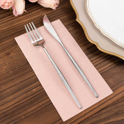 Silver fork and knife on a pink napkin, with a decorative plate in the background.