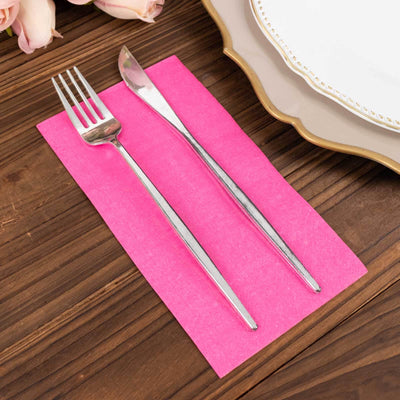 Silver fork and knife on a pink napkin against a wooden table.