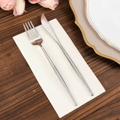 Silver fork and knife on a napkin beside a decorative plate.