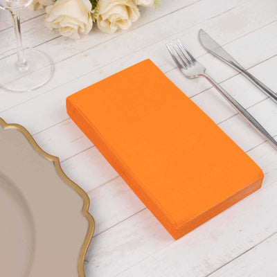 Orange napkins stacked on a white wooden table with dining utensils.