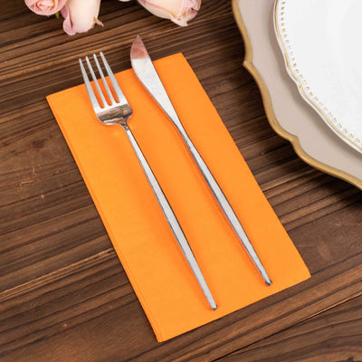 Orange napkin with silver fork and knife on a wooden table.