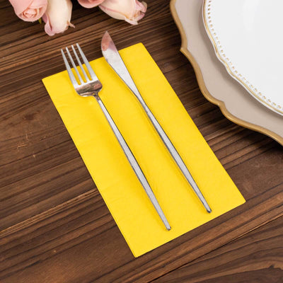 Yellow napkin with silver fork and knife on a wooden table.