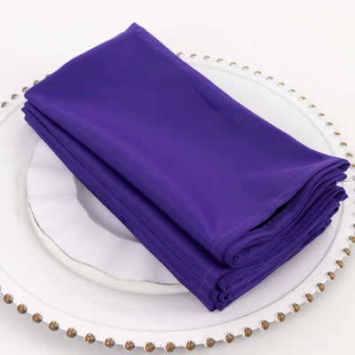 Purple cloth napkins neatly stacked on a decorative plate.
