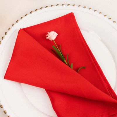 Red napkin elegantly folded with a pink flower on a plate.