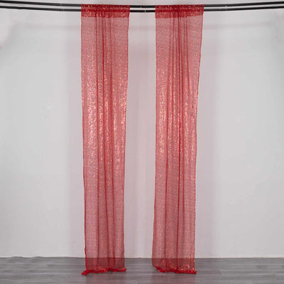 Red sheer curtains hanging from a rod against a plain backdrop.