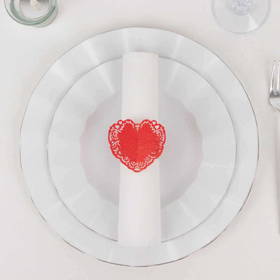 Red heart napkin ring on white plates for elegant table setting.