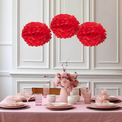 Red tissue paper pom poms hanging above a beautifully set dining table.