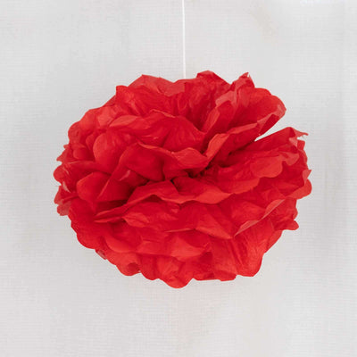 Red tissue paper pom pom decoration hanging on a white background.