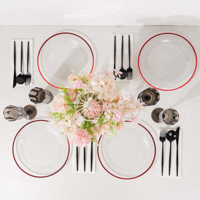 Elegant dining setup with clear plates, black cutlery, and floral centerpiece.