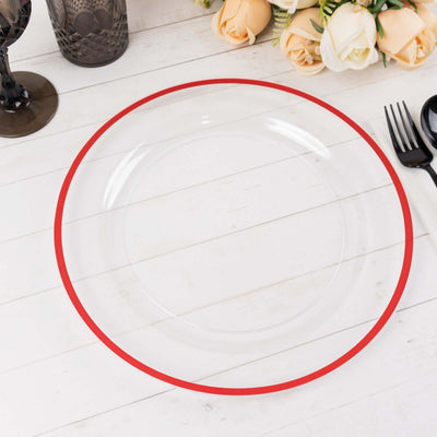 Clear plate with red rim on a wooden table surrounded by flowers and utensils.