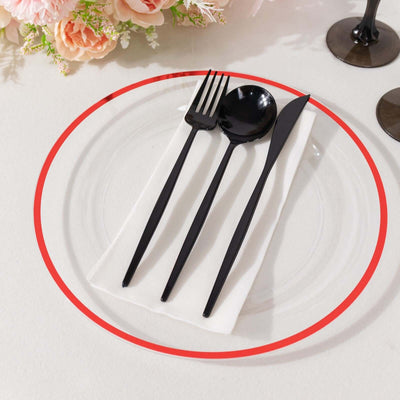 Black cutlery set on a clear plate with white napkin and floral decor.