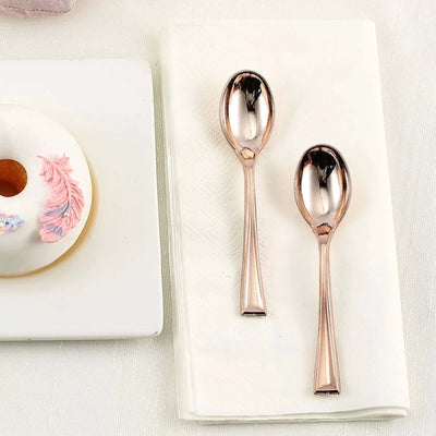 Two elegant rose gold teaspoons on a napkin beside a decorated donut.