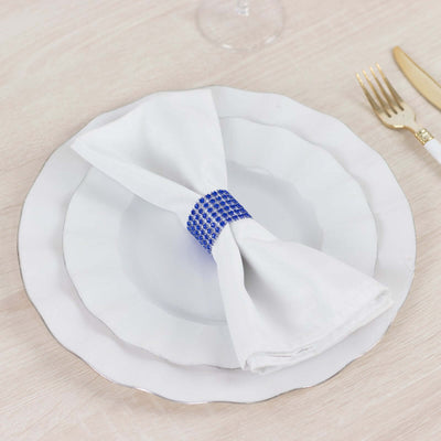 White napkin with blue rhinestone ring on elegant plate setting.