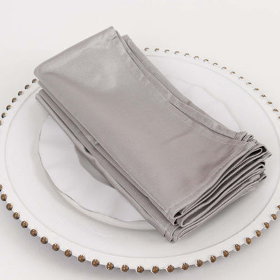 Set of elegant silver satin napkins stacked on a decorative plate.
