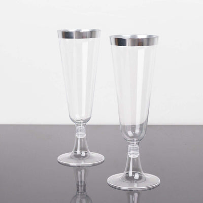 Clear plastic champagne flutes with silver rims on a plain background