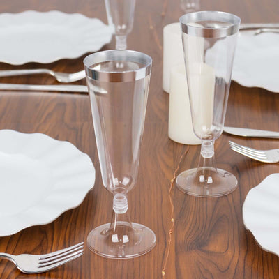 Clear plastic champagne flutes on a wooden table with white plates and candles.