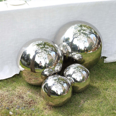 Reflective metal spheres arranged on grass in a garden setting.
