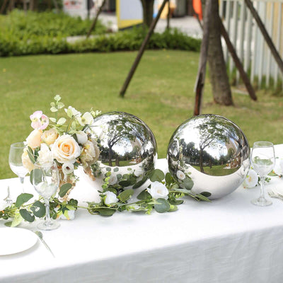 Decorative silver spheres with flowers on a table in an outdoor setting.