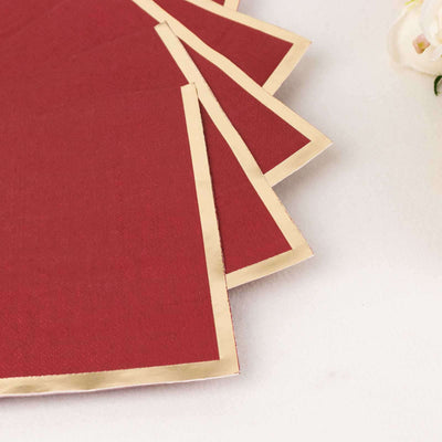 Red fabric napkins with gold trim, neatly stacked on a white surface.