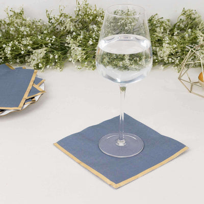 Navy napkin with gold trim under a glass of water on a white table.