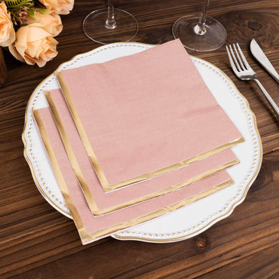 Pink napkins with gold trim on an elegant plate, set on a wooden table.
