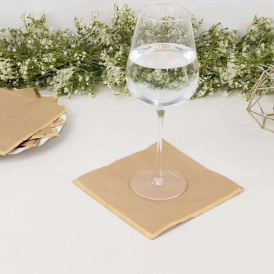 Glass of water on a gold napkin with greenery in the background.