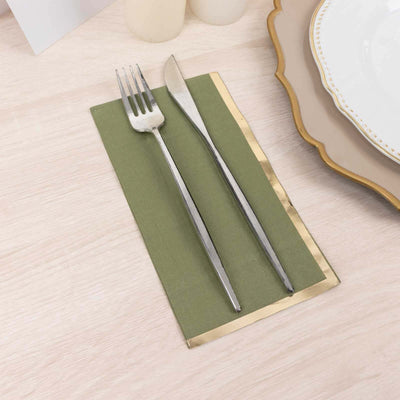 Silver fork and knife on a green napkin with gold trim on a wooden table.