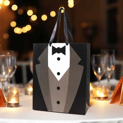 Tuxedo gift bag on a table with candles and blurred lights in the background.